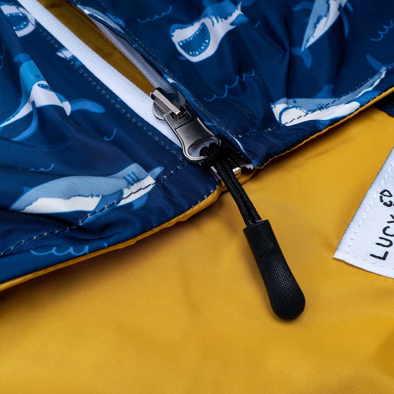 Close-up of a zipper on a blue jacket with shark pattern, on a yellow background.