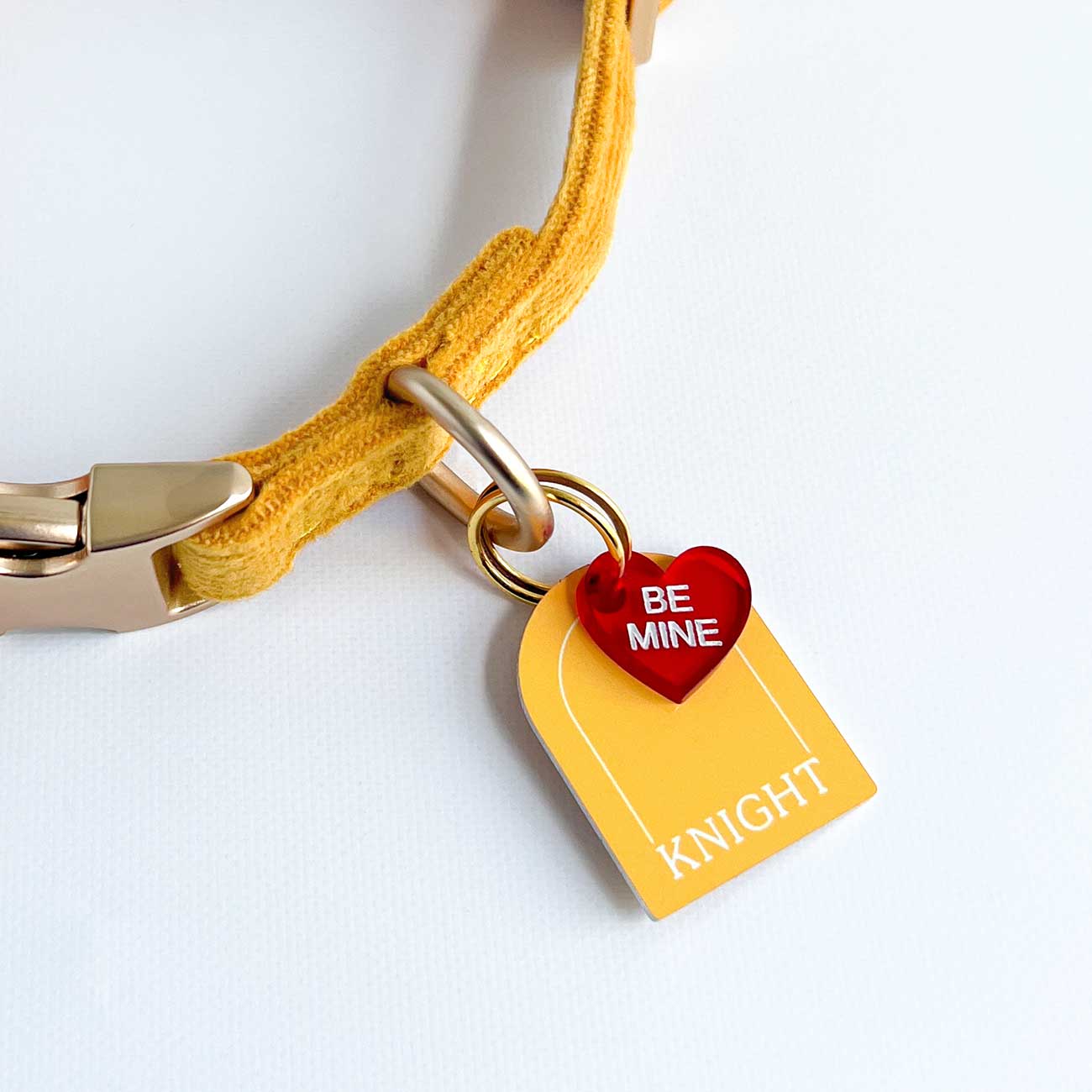 Yellow dog collar with a red 'Be Mine' heart tag on a white background