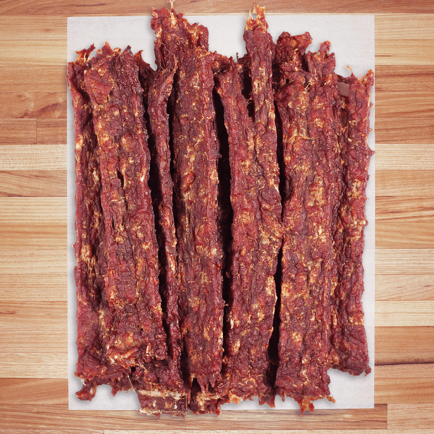 Dried boar jerky strips on a white paper towel over a wooden surface