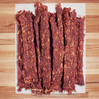 Dried boar jerky strips on a white paper towel over a wooden surface