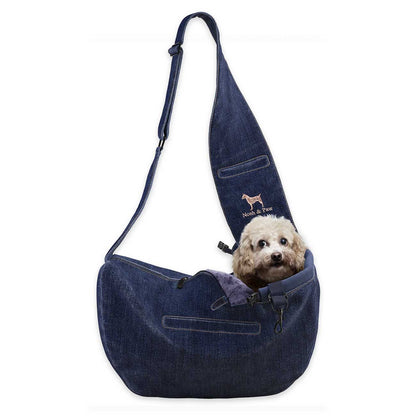 Dog inside a dark blue denim sling bag with a visible brand logo on a white background