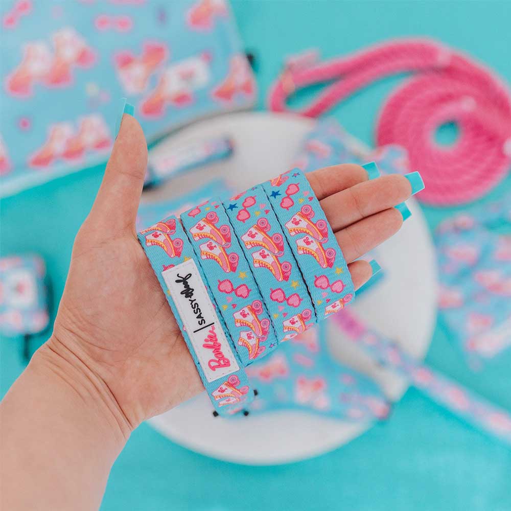 Hand holding colorful shoelaces with a Barbie logo against a blue background