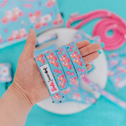 Hand holding colorful shoelaces with a Barbie logo against a blue background