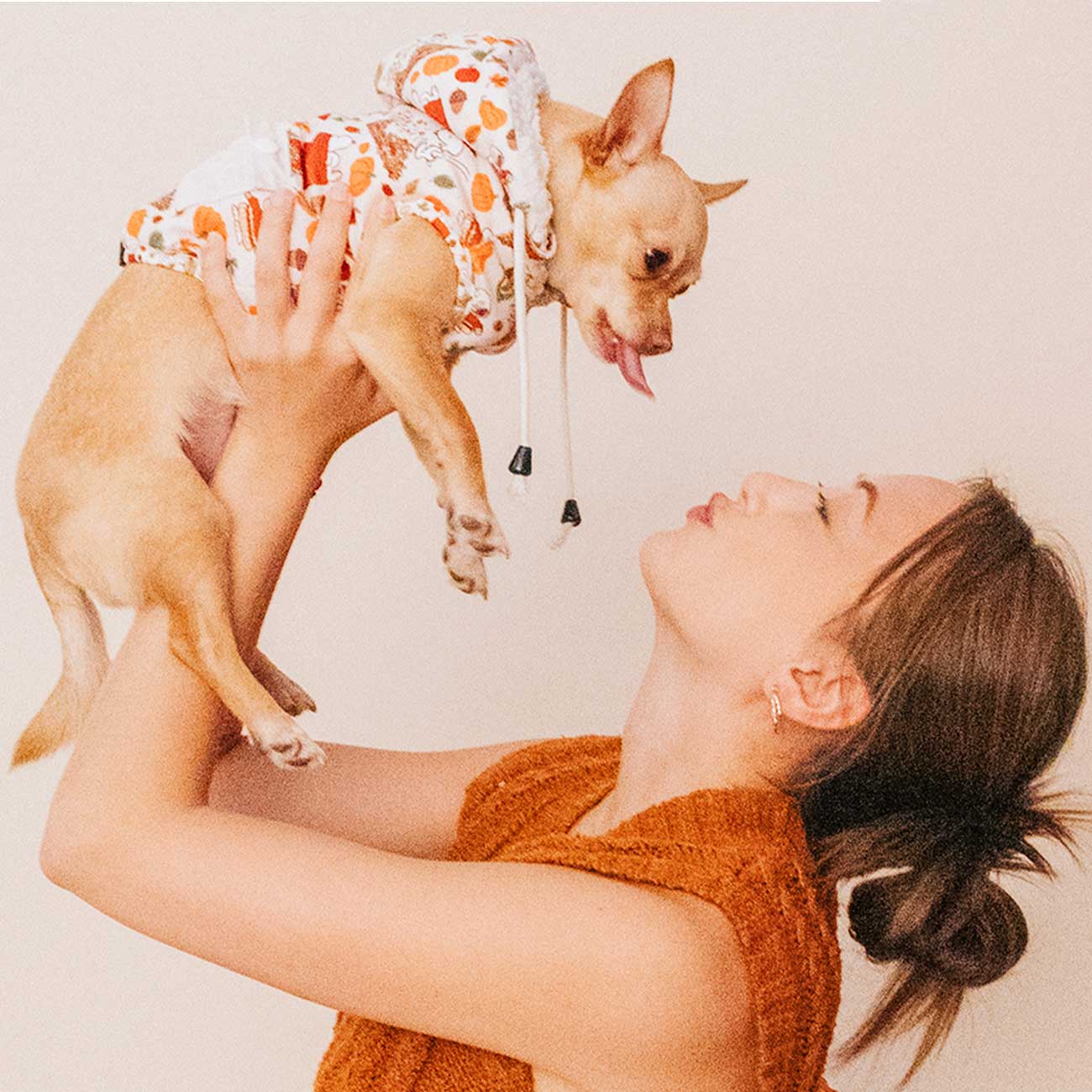 Woman holding a small dog wearing a hoodie against a plain background