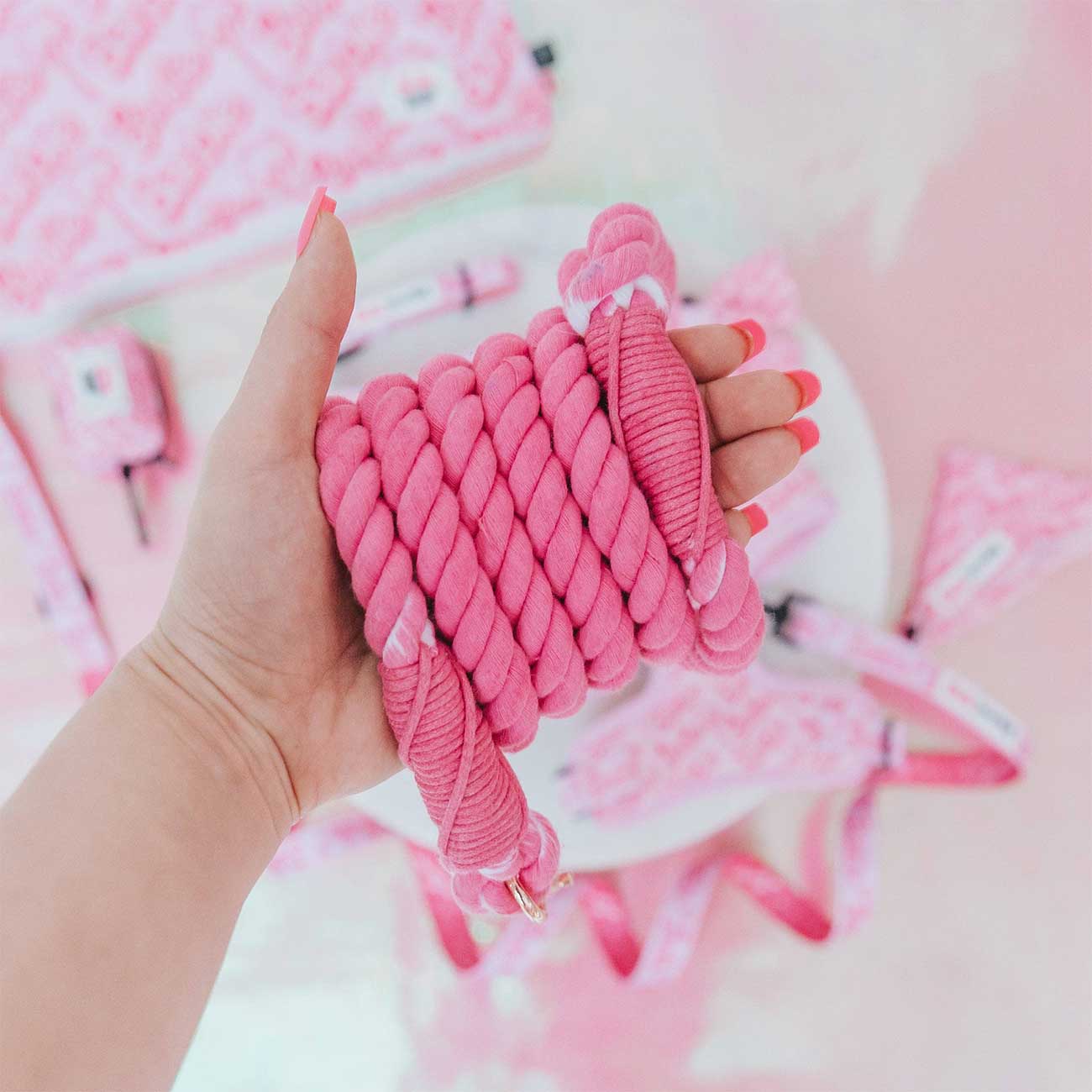 Hand holding a pink braided rope with a soft pink background