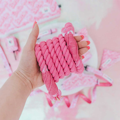 Hand holding a pink braided rope with a soft pink background
