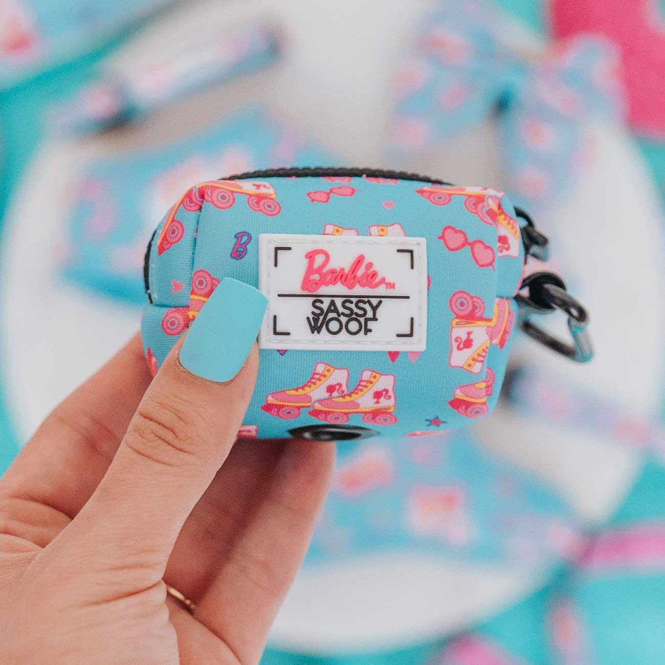 Small blue dog waste bag holder with pink patterns held by a hand against a colorful background