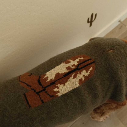 Dog wearing a sweater with a brown and beige pattern on a light-colored floor.