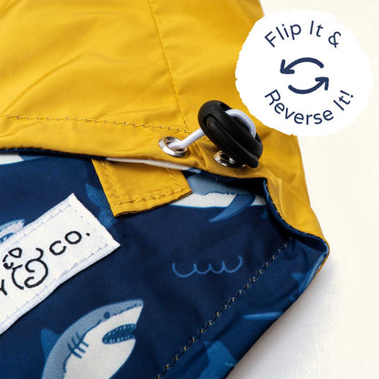 Close-up of a reversible jacket with yellow and blue sides, featuring a shark design, and a label with text.
