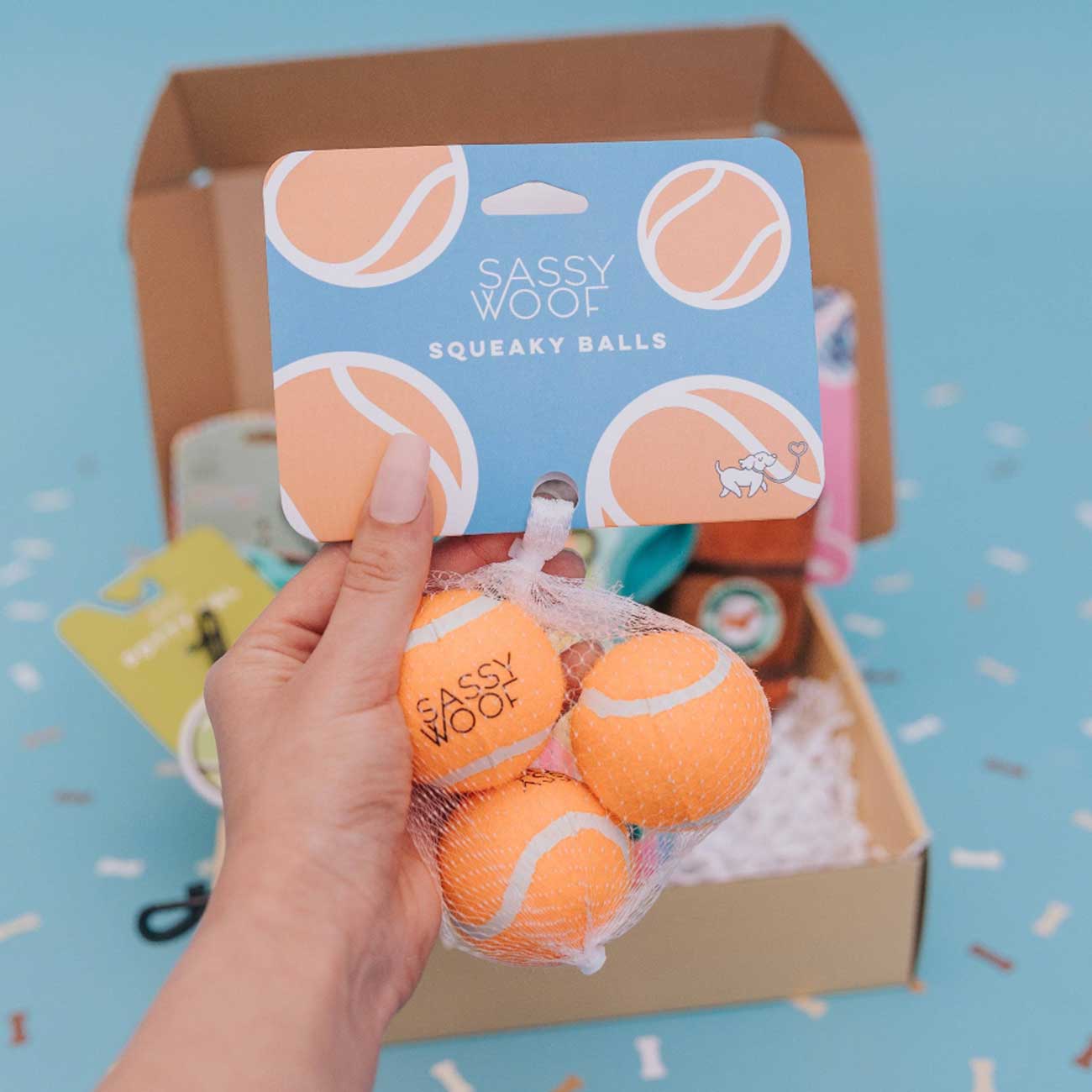 Hand holding Sassy Woof squeaky balls with packaging in the background