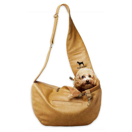 Tan leather pet sling bag with a small dog inside on a white background